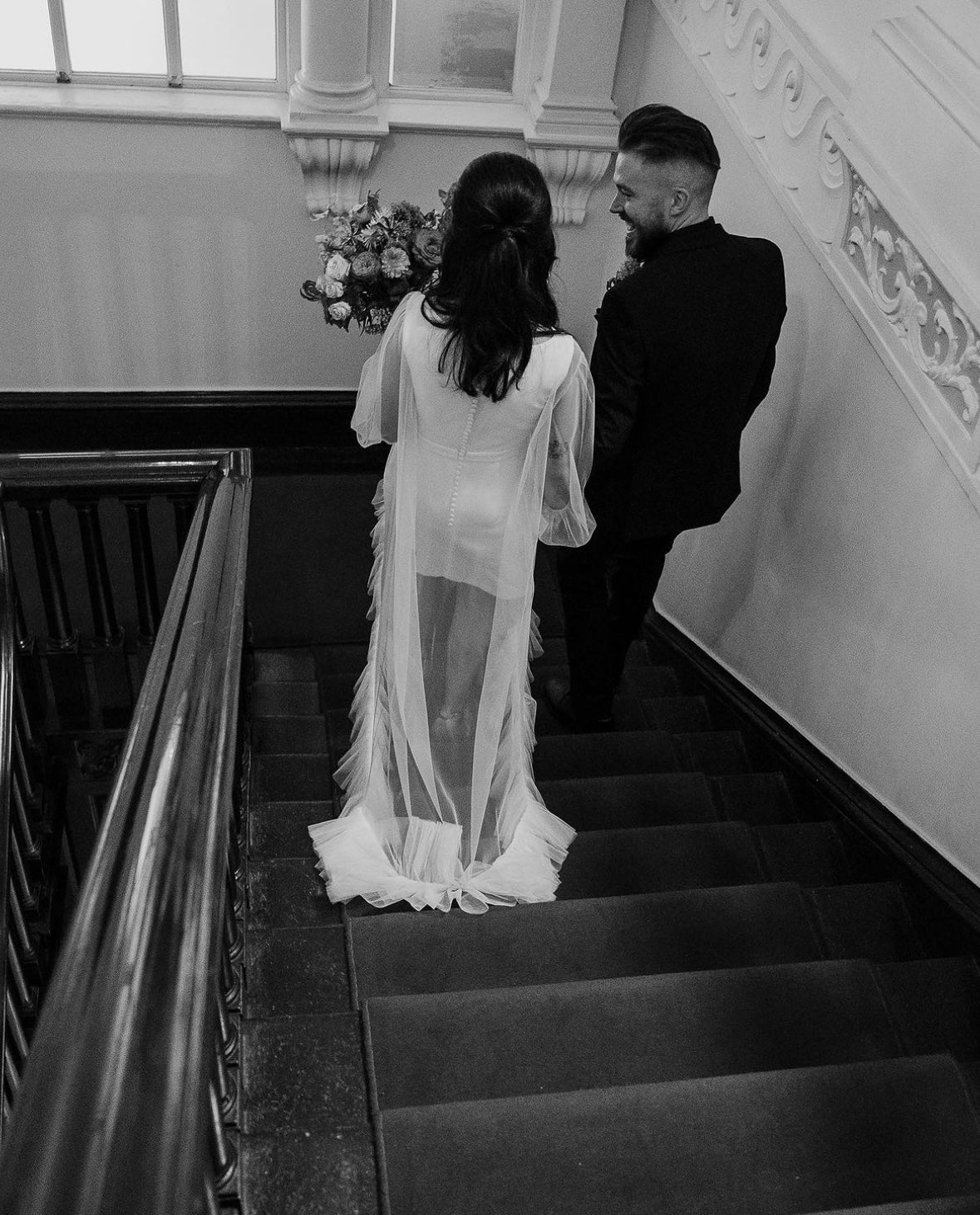 Amy and Gar on the staircase at City Hall, Dublin. Amy wears a crepe shift dress under a sheer tulle overdress with a ruffled hem.