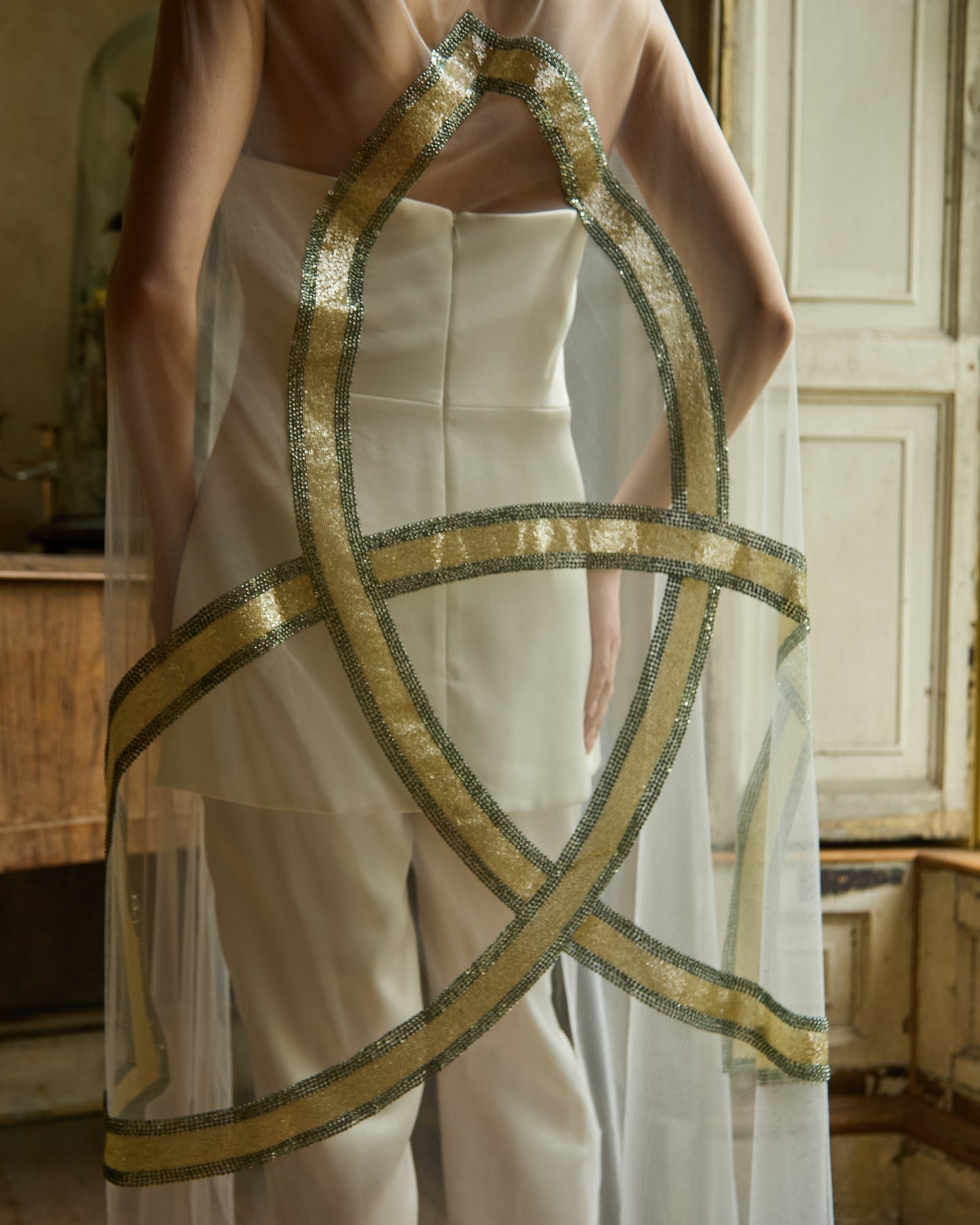 Bride in minimalist white jumpsuit wearing sheer tulle bridal cape with gold Celtic trinity knot design by Mizz Rio, modern alternative wedding look in Dublin