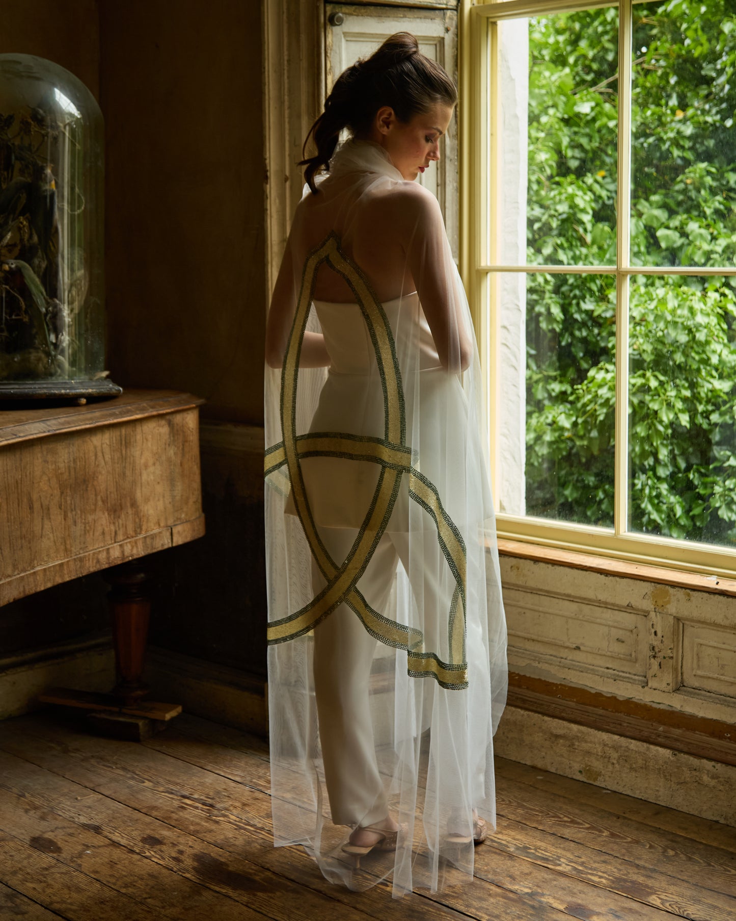 Bride in minimalist white jumpsuit wearing sheer tulle bridal cape with gold Celtic trinity knot design by Mizz Rio, modern alternative wedding look in Dublin